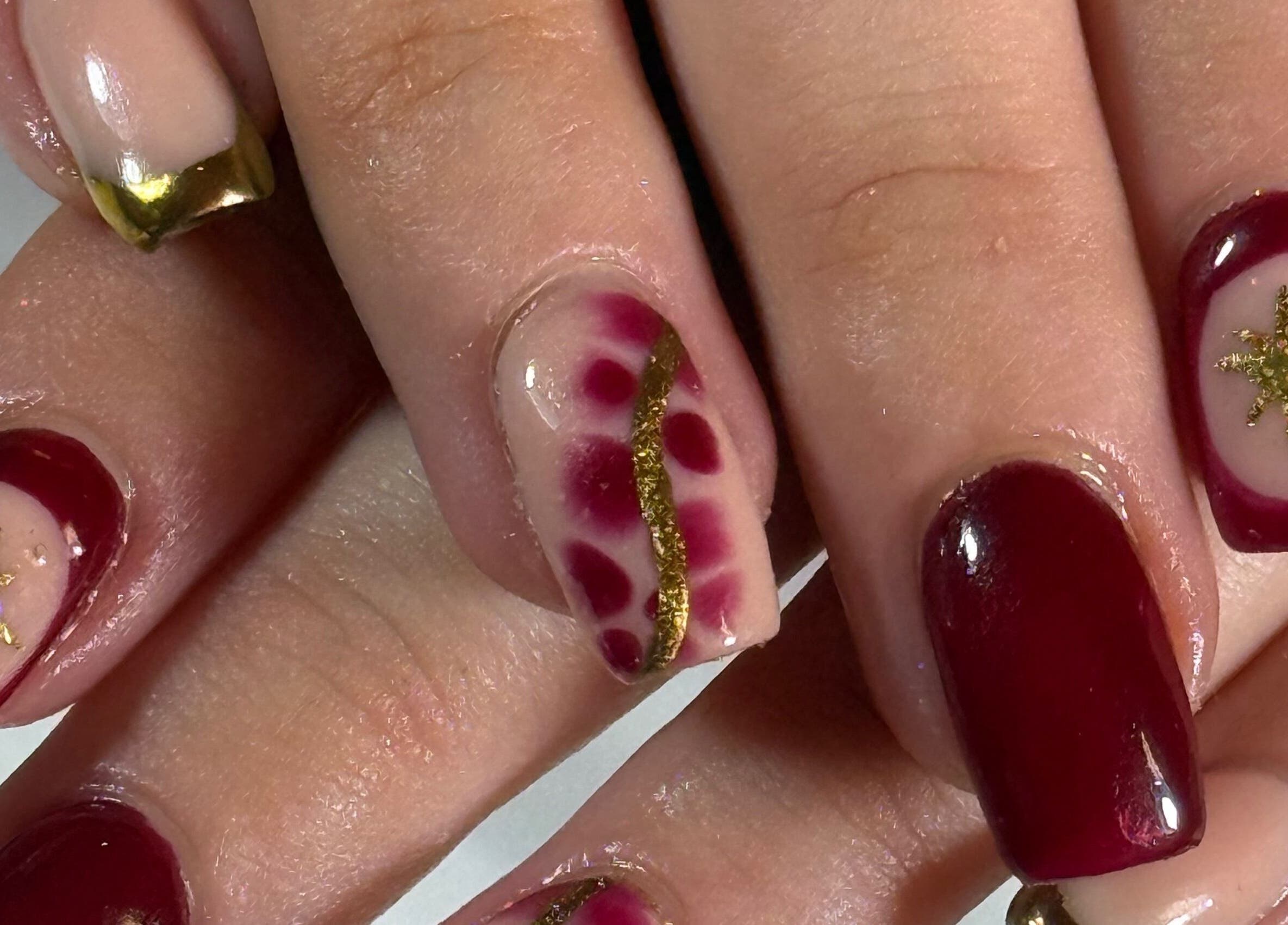 Elegant nail art at The Luxury Nail Bar, Galashiels, Scotland, GB showcasing gold accents and rich red polish.