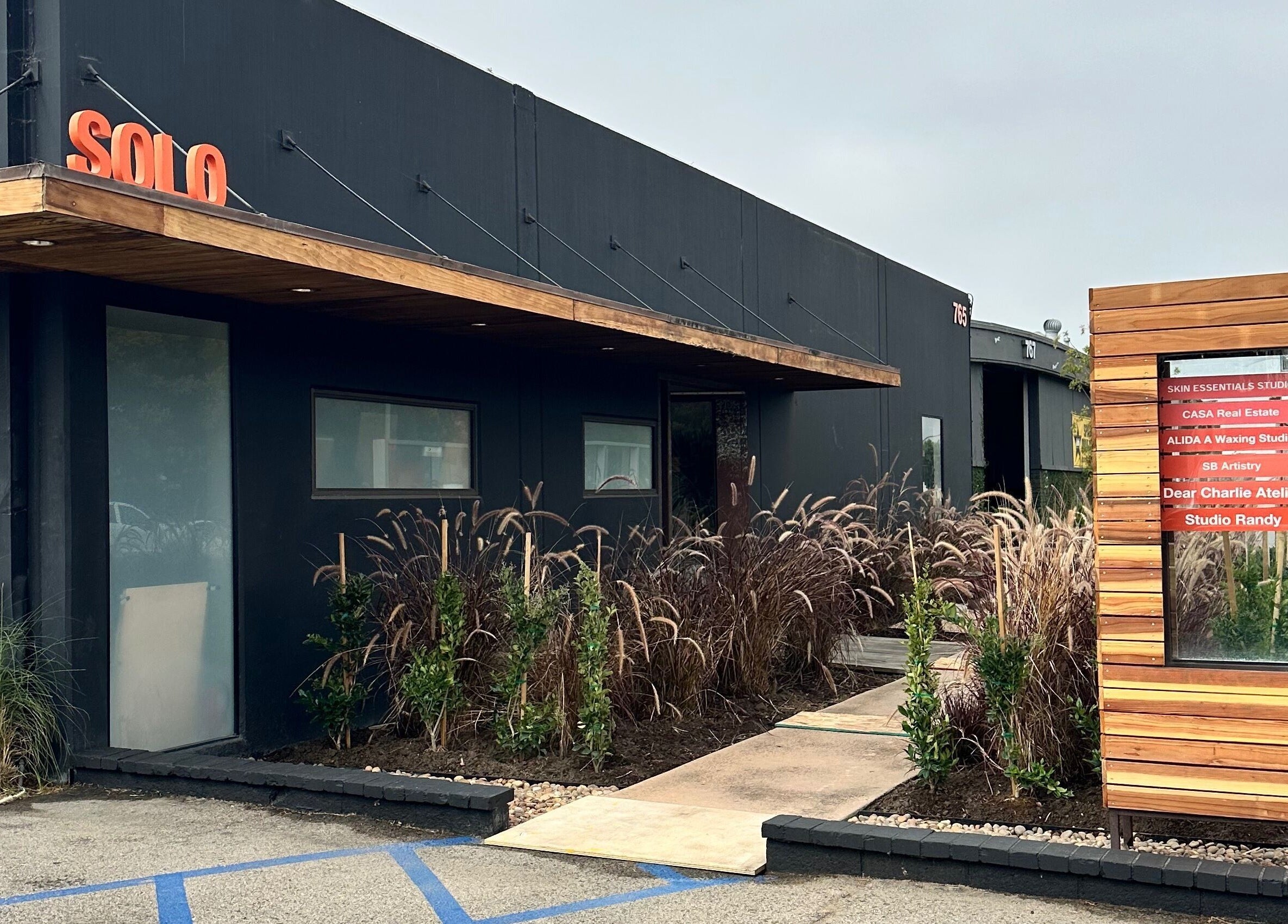 Front entrance of SB Artistry in Costa Mesa, California, US, showcasing modern exterior design and lush landscaping.