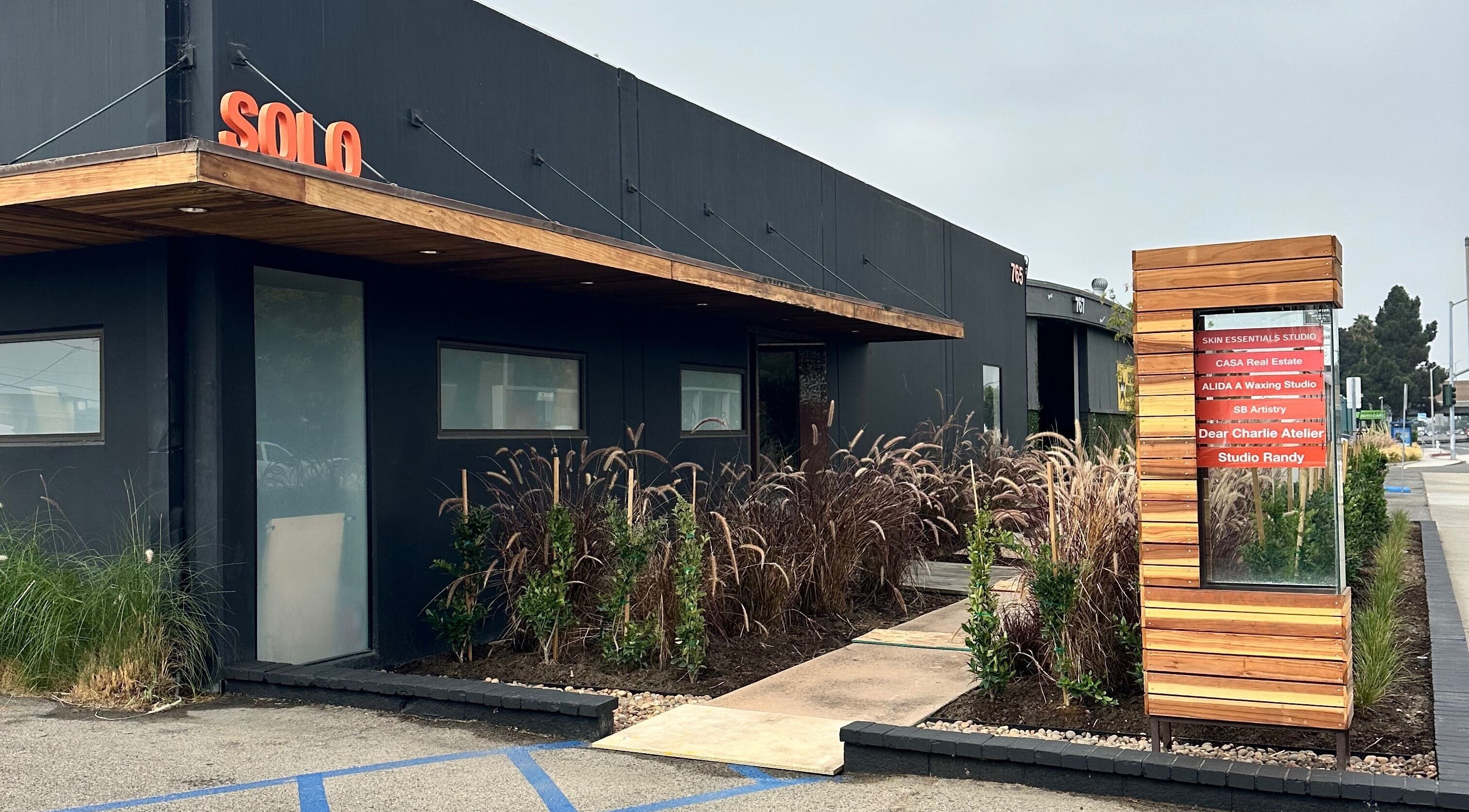 Front entrance of SB Artistry in Costa Mesa, California, US, showcasing modern exterior design and lush landscaping.