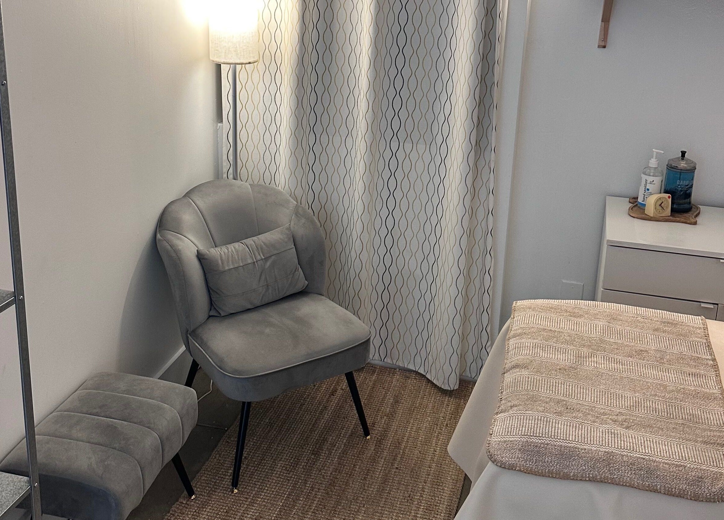 Cozy relaxation area at SB Artistry, Costa Mesa, California, US, featuring a plush chair and spa essentials.