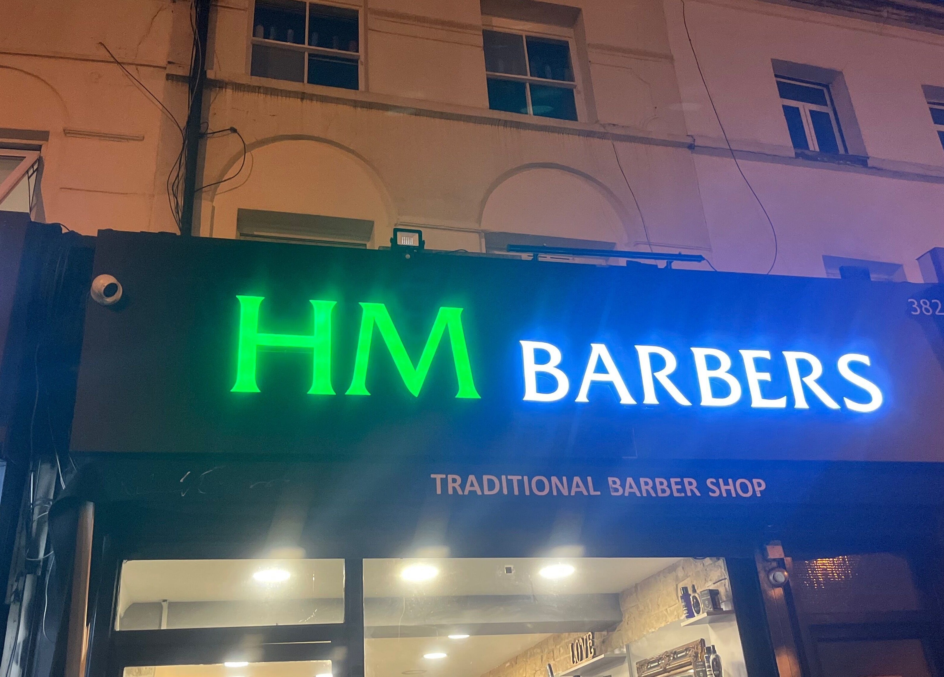HM Barbers glowing sign at night, London, England, GB. Traditional Barber Shop in vibrant lights.