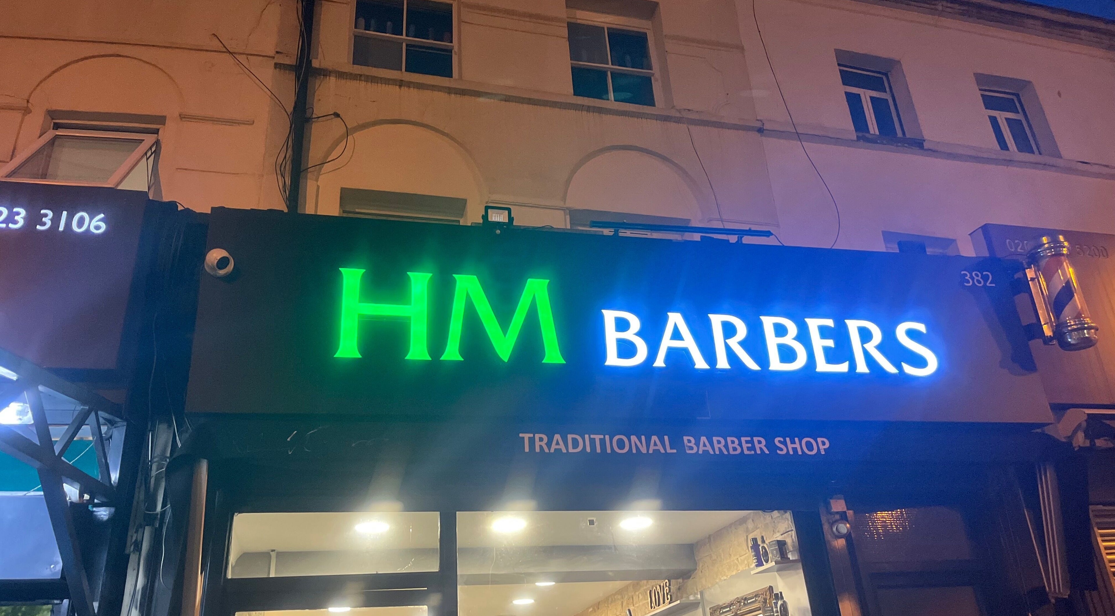 HM Barbers glowing sign at night, London, England, GB. Traditional Barber Shop in vibrant lights.