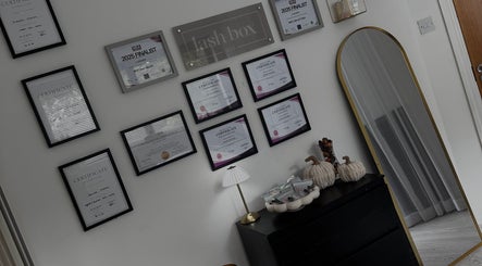 Award-adorned wall at Lash Box Mcr, Greenmount, England, showcasing certificates of excellence.