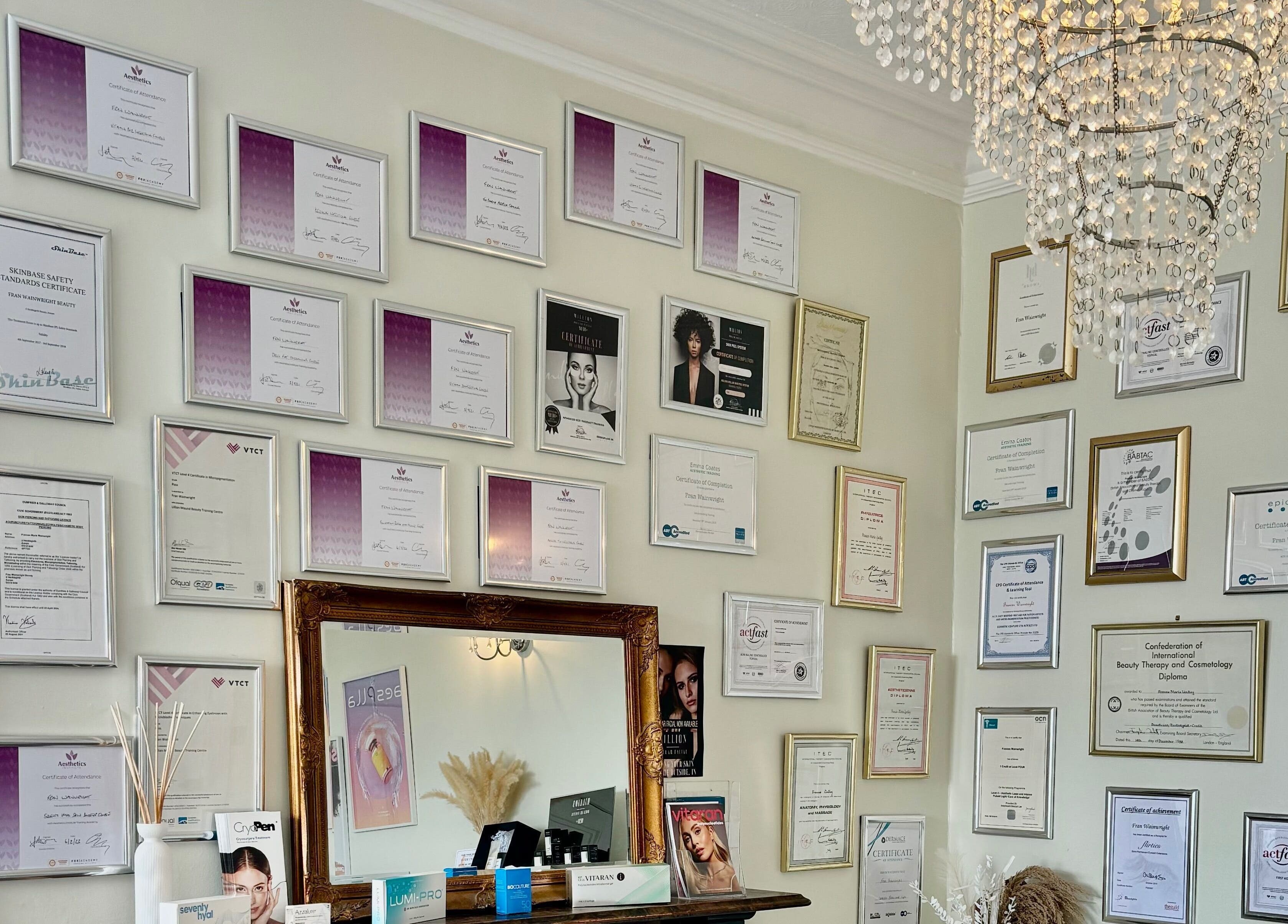 Certificate wall at Fran Wainwright Beauty and Aesthetics, Annan, Scotland, GB under a chandelier.