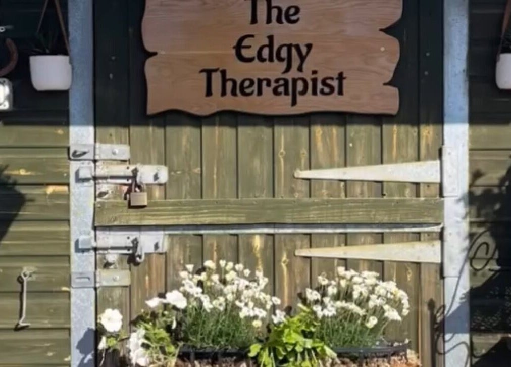 Entrance to The Edgy Therapist @ The Holistic Hideaway, Broadclyst, England, with wooden sign and flowers.