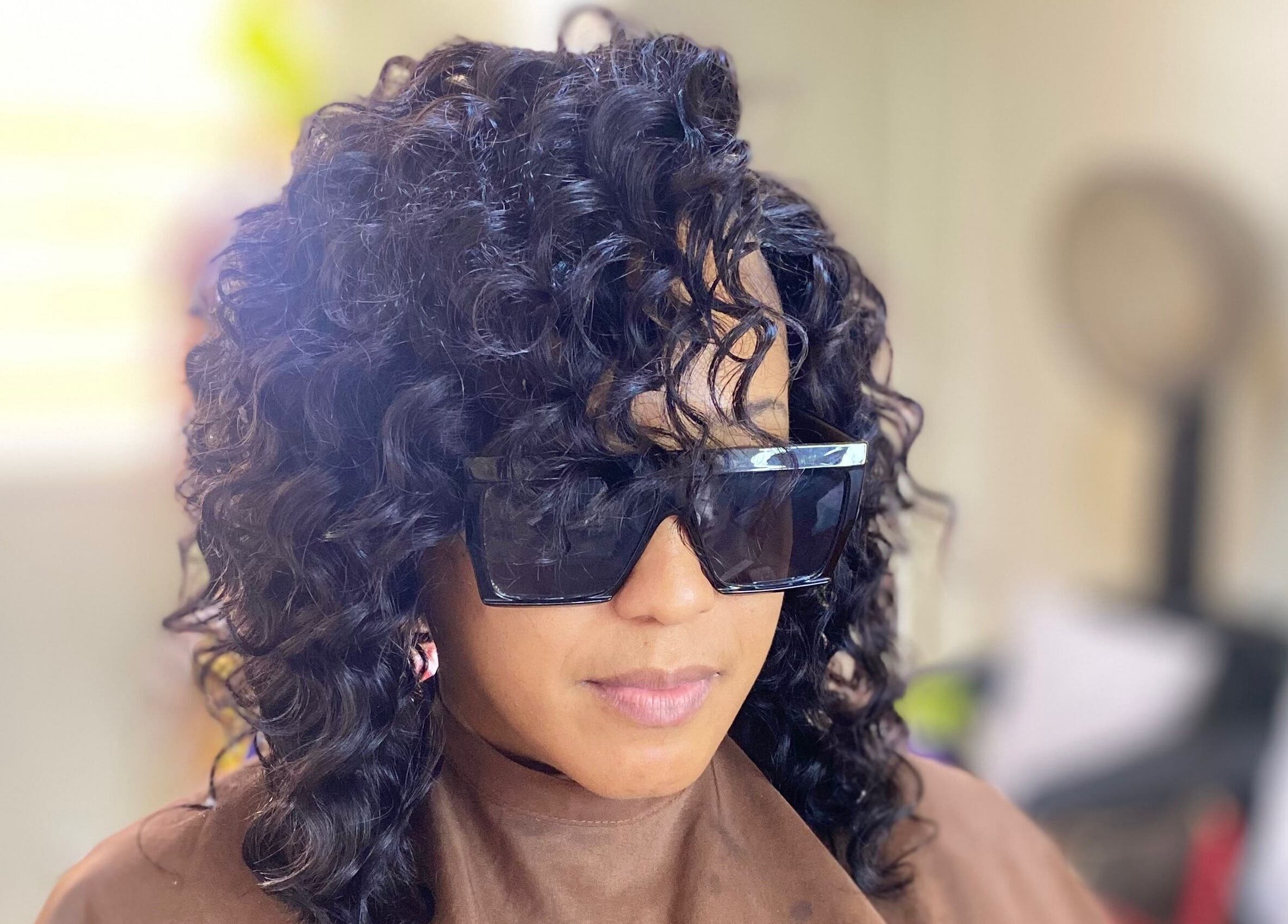 Stylish woman with curly hair at Haus Of Lisa J, Bridgetown, Saint Michael, BB, showcasing sleek sunglasses.