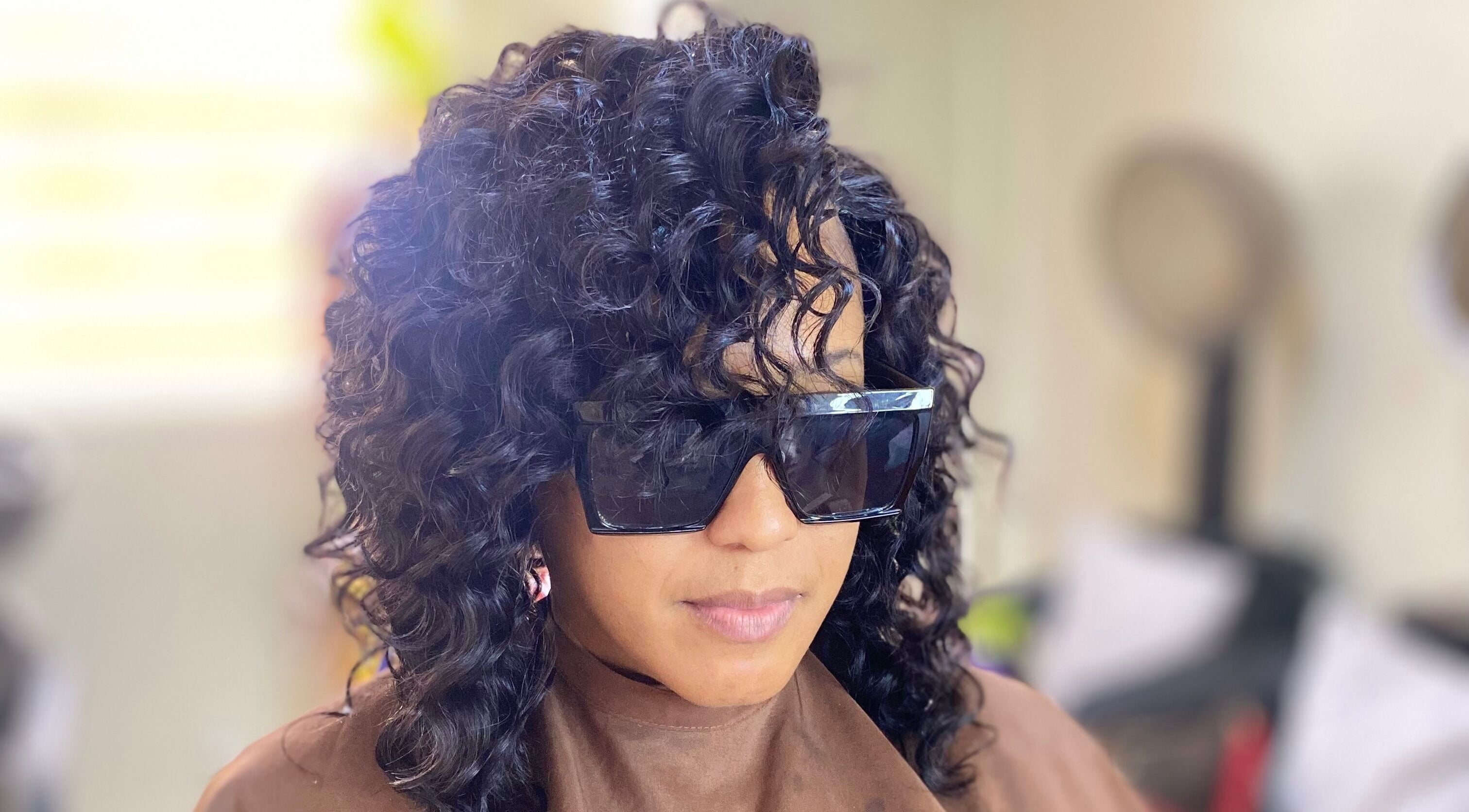 Stylish woman with curly hair at Haus Of Lisa J, Bridgetown, Saint Michael, BB, showcasing sleek sunglasses.