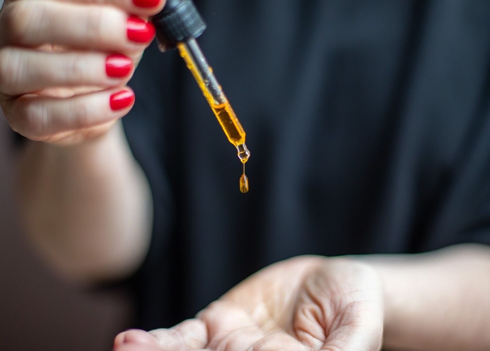 A hand holds a dropper of golden oil at The Tides in Leeds, GB, offering a soothing wellness experience.