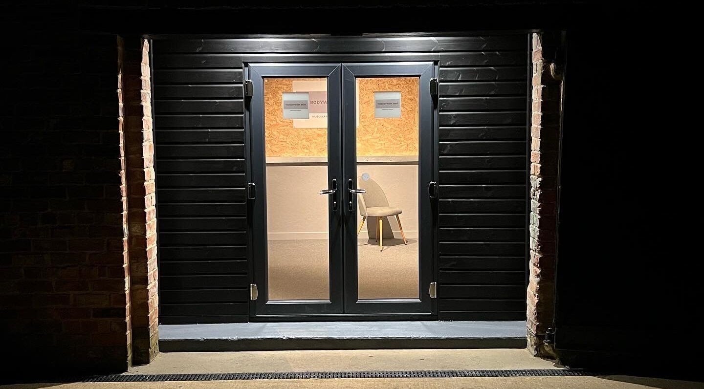 The inviting entrance of The Bodywork Barn in Louth, England, GB, warmly lit with a view of the interior.