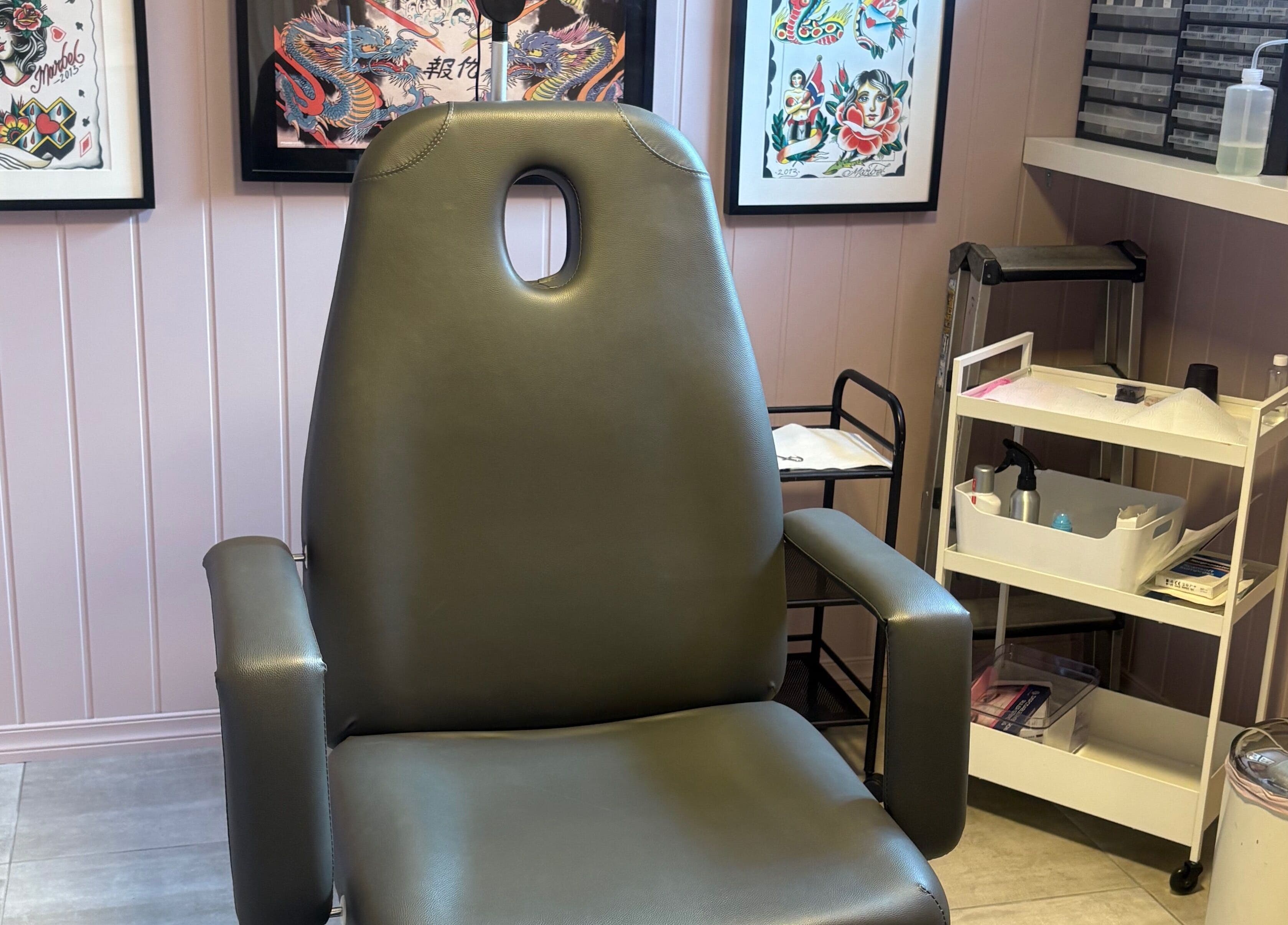 Komfortabel stol i Tattoo Tom Studio i Sørumsand, Akershus, NO, omgitt av kunstverk og verktøy.