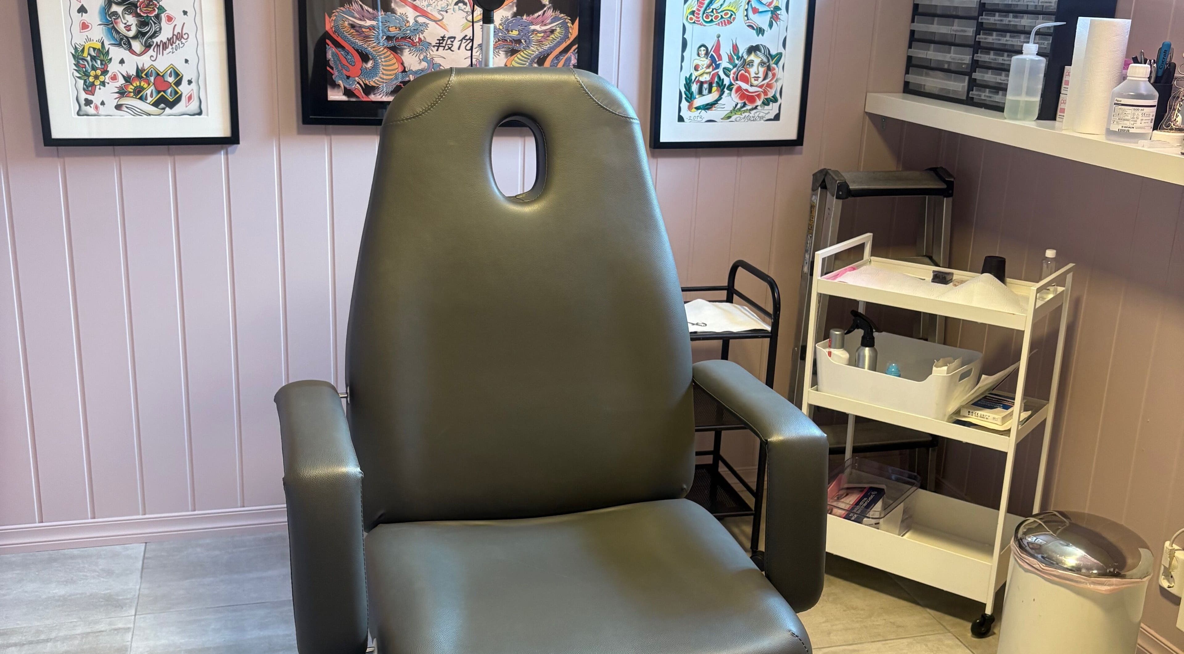 Komfortabel stol i Tattoo Tom Studio i Sørumsand, Akershus, NO, omgitt av kunstverk og verktøy.