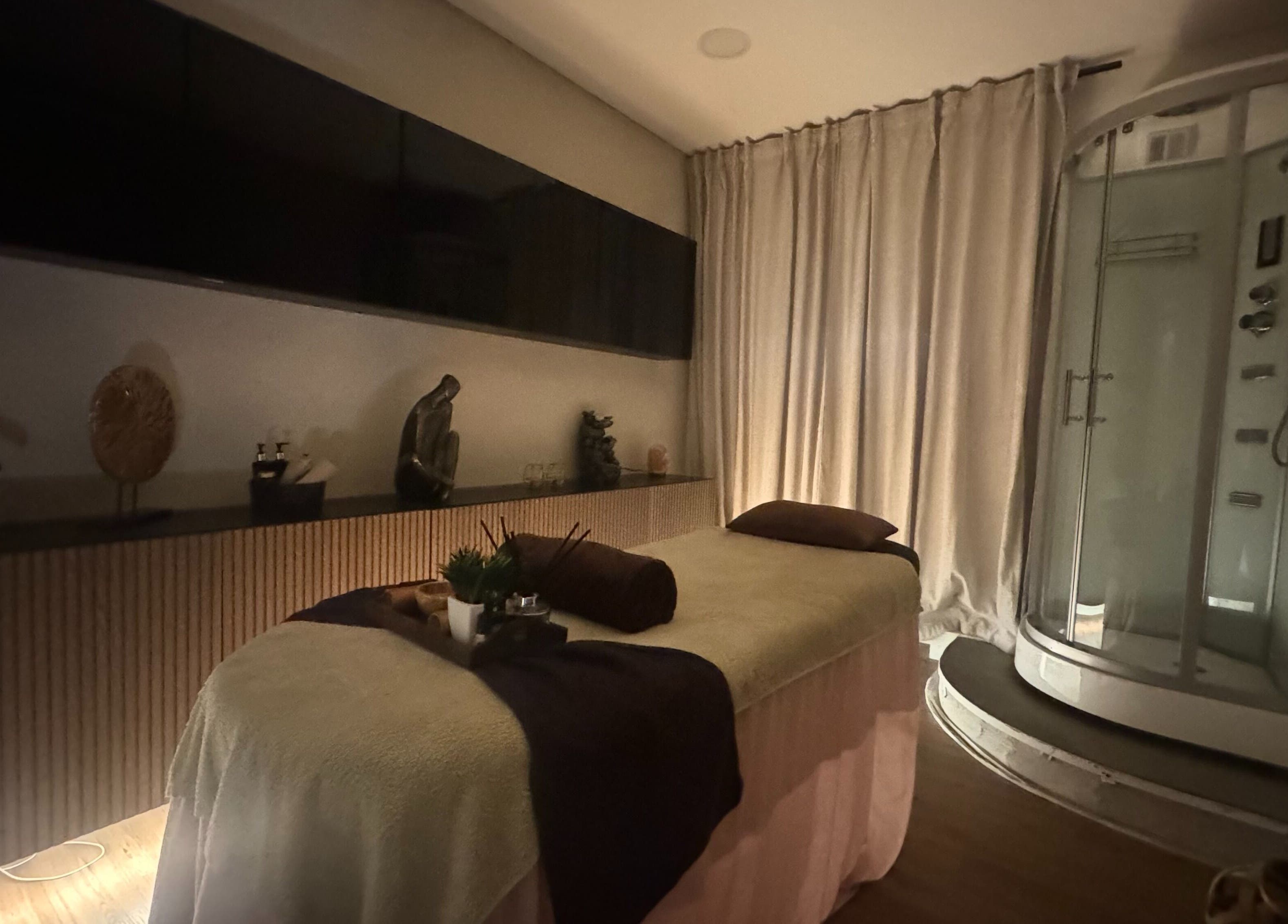 Sala de tratamento relaxante em The Spa Experience, Cascais, Lisboa, PT, com mesa de massagem e chuveiro.