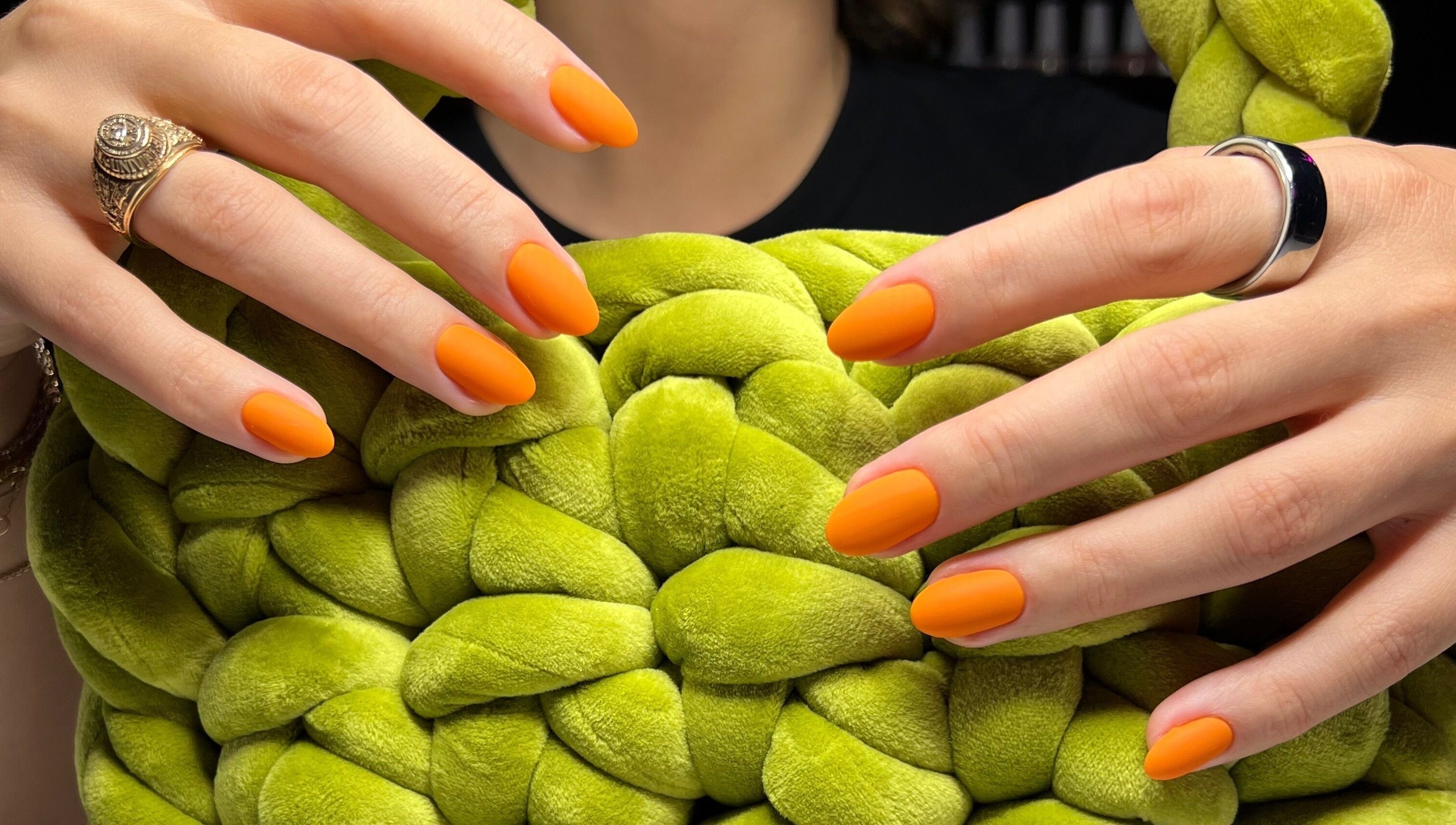 Bright orange manicured nails at Nail Standards, Austin, Texas, US against a green textured backdrop.
