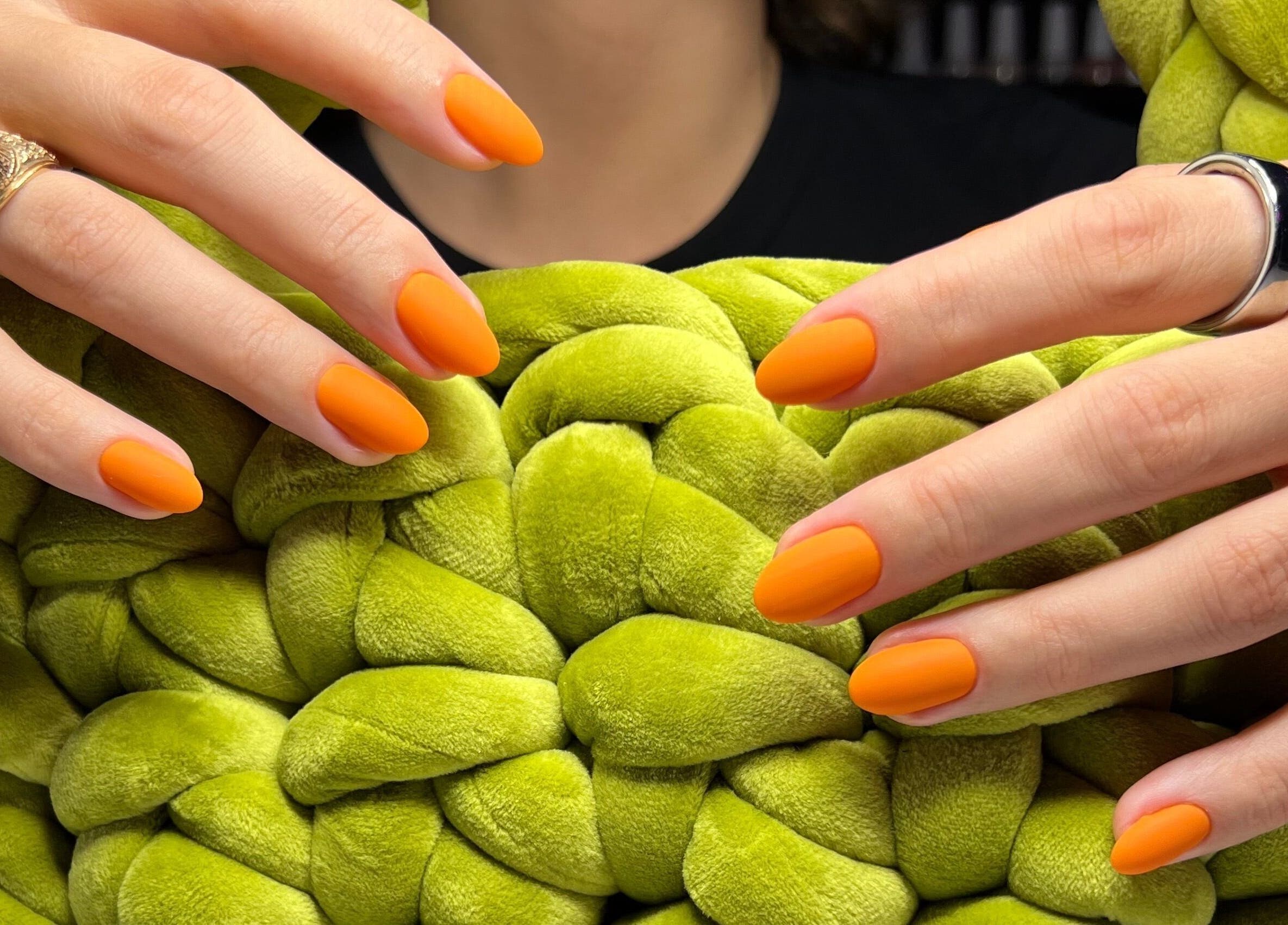 Bright orange manicured nails at Nail Standards, Austin, Texas, US against a green textured backdrop.