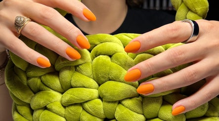 Bright orange manicured nails at Nail Standards, Austin, Texas, US against a green textured backdrop.