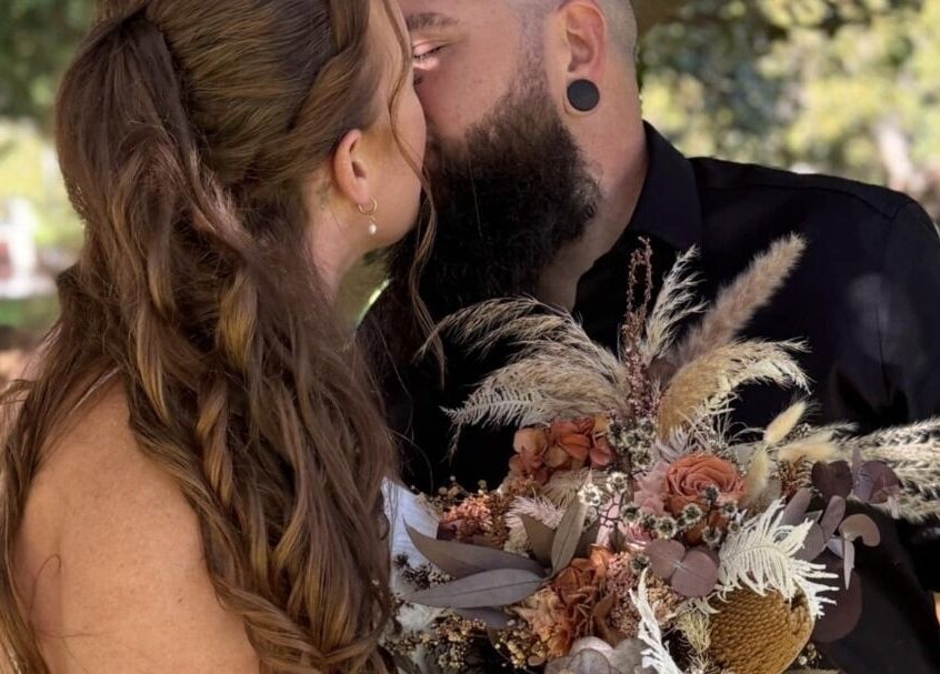 Couple shares a tender kiss at Glow Tribe Spray Tanning, Glen Forrest, Western Australia, AU, holding floral bouquet.