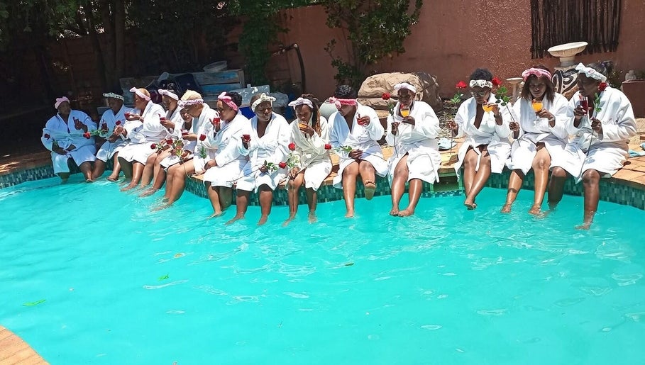 Group enjoying poolside robes at Bohl Squared Beauty Spa, Springs, Gauteng, ZA, holding roses and drinks.
