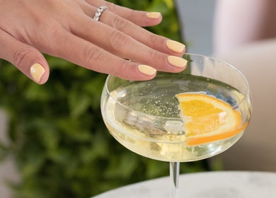 Mano con manicura amarilla toca copa con rodaja de naranja en Glow Haus GT, Ciudad De Guatemala, Guatemala, GT.
