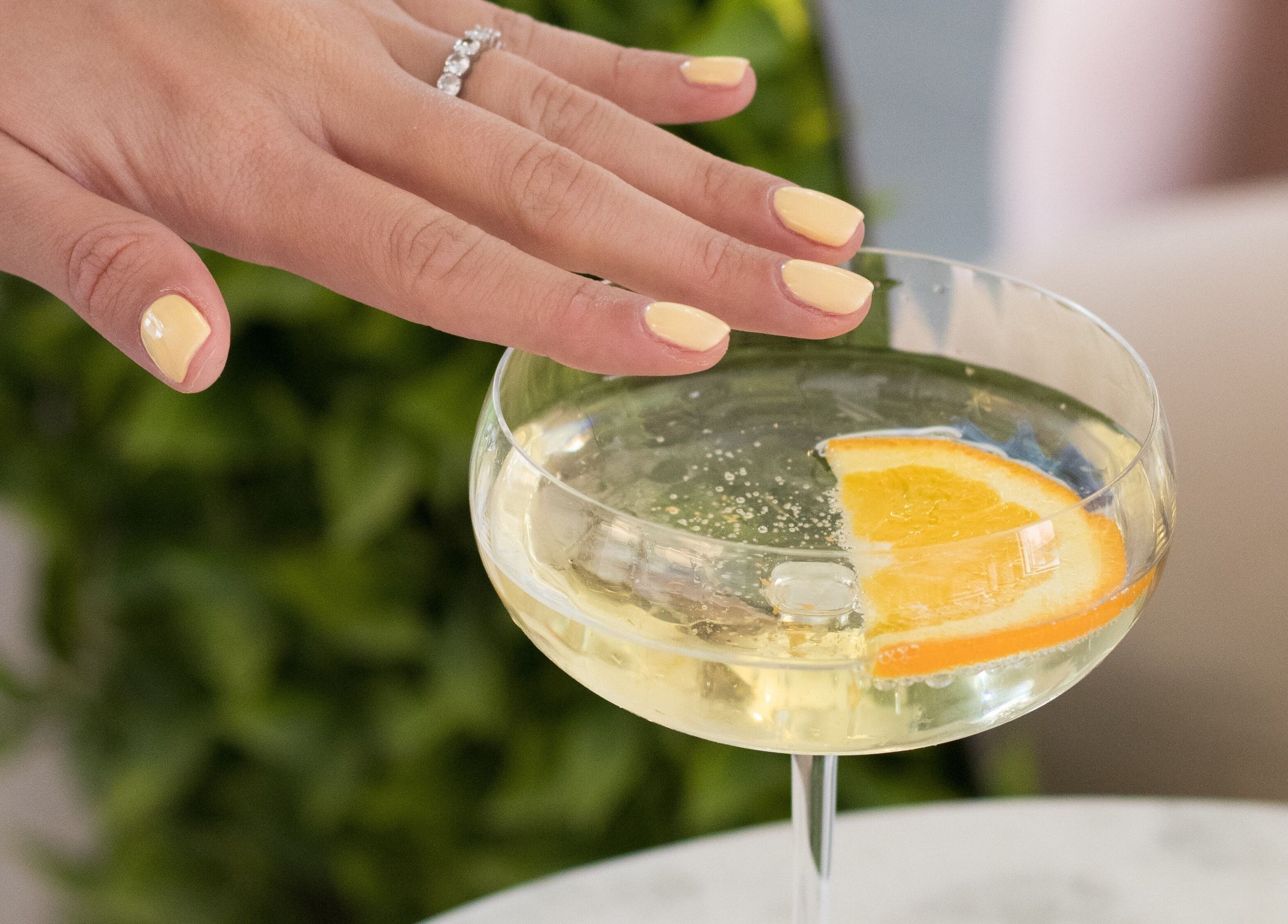 Mano con manicura amarilla toca copa con rodaja de naranja en Glow Haus GT, Ciudad De Guatemala, Guatemala, GT.