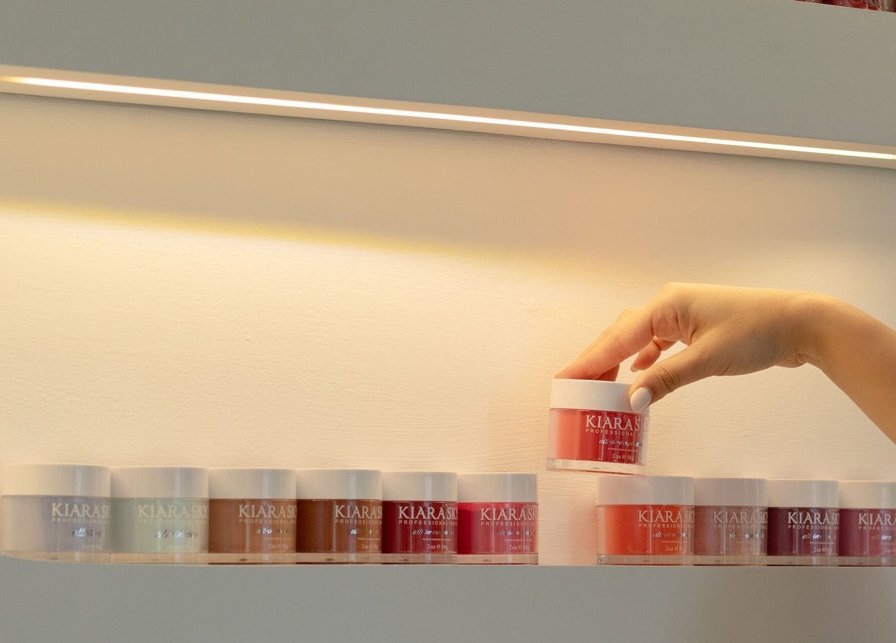 Estante de esmaltes en Glow Haus GT, Ciudad De Guatemala, Guatemala, GT. Mano seleccionando tono rojo.