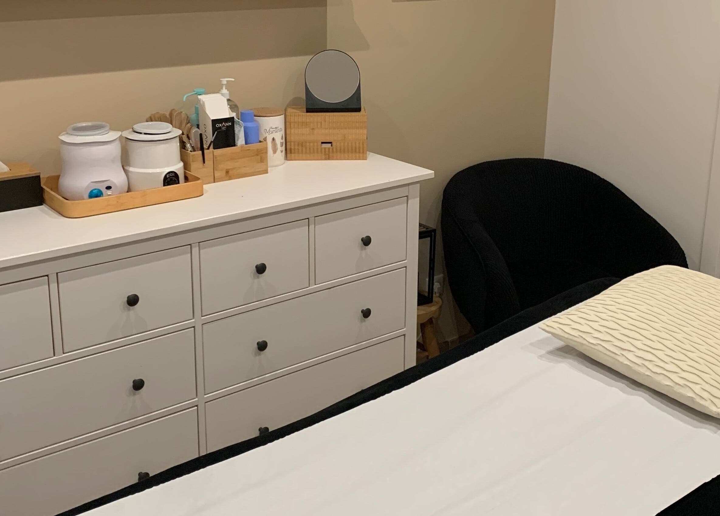 Salle de soin sereine à Studio Beauté by Julie, Théville, Normandie, FR avec table et commode bien rangée.