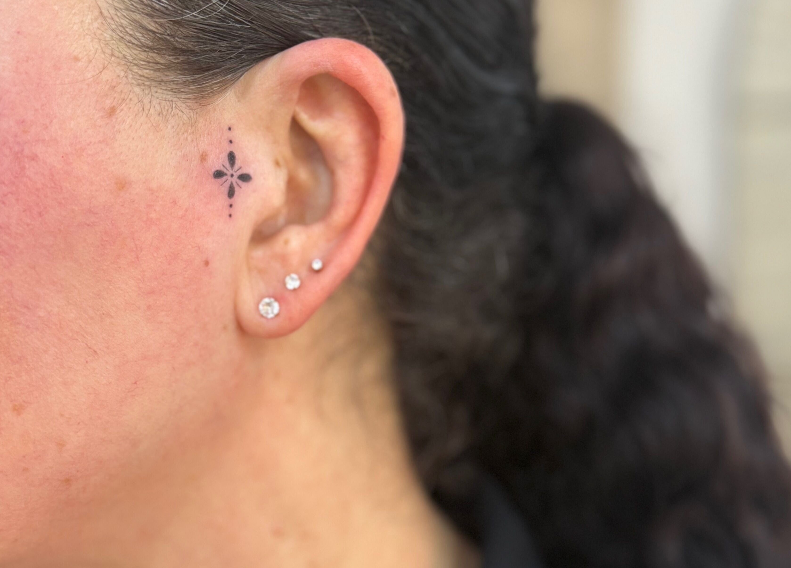 Stylish ear tattoo at Adara Ink in Chadderton, England, GB showing detailed floral design near piercings.