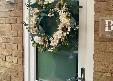 Elegant floral wreath decorates the door of Brows & Beauty by Georgia in Effingham, England, GB.