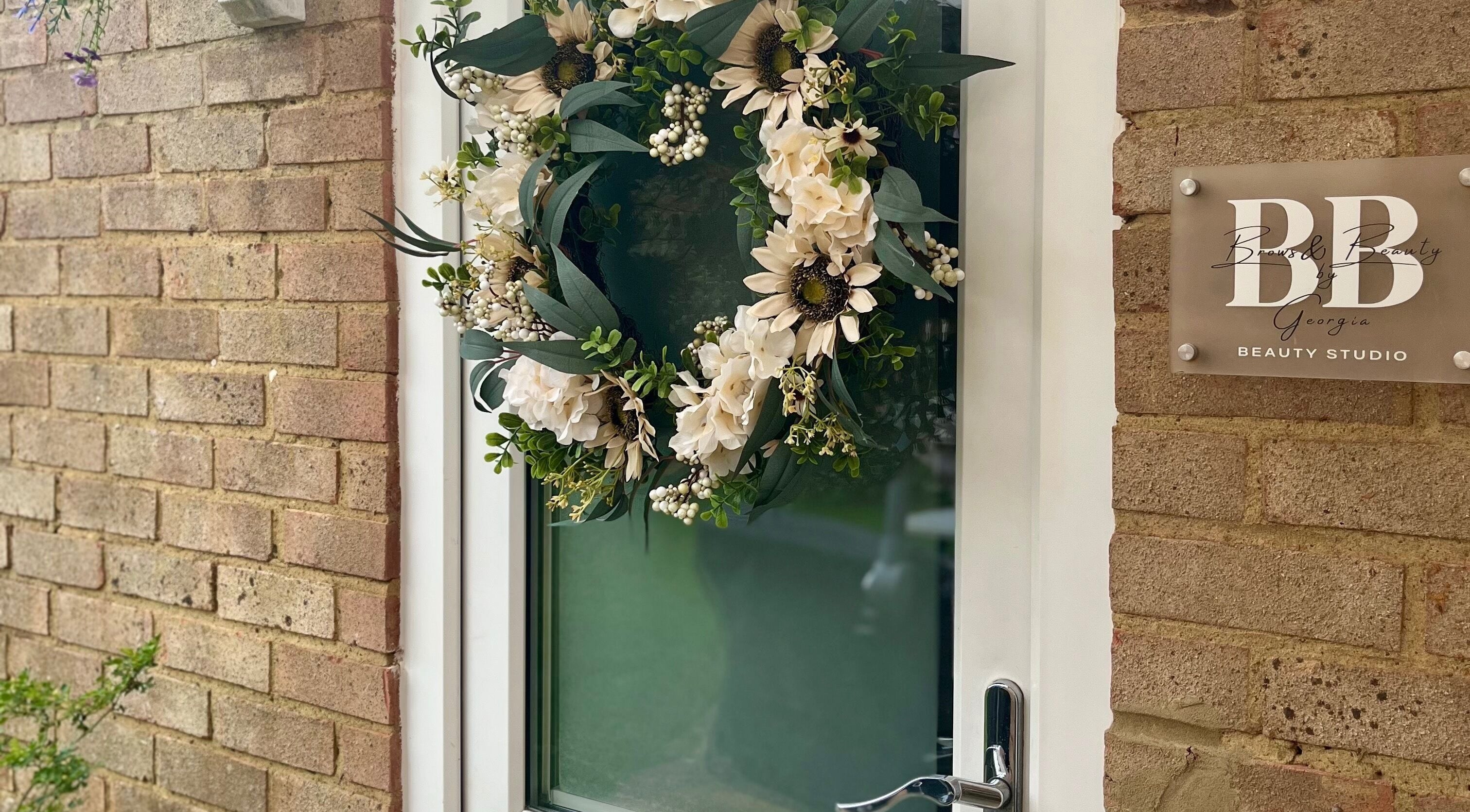 Elegant floral wreath decorates the door of Brows & Beauty by Georgia in Effingham, England, GB.