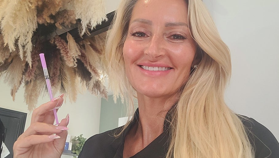 Beauty expert at Cupids Glow in Bolton, England, GB holding a beauty tool smiling amid elegant decor.