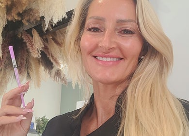 Beauty expert at Cupids Glow in Bolton, England, GB holding a beauty tool smiling amid elegant decor.
