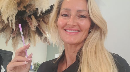Beauty expert at Cupids Glow in Bolton, England, GB holding a beauty tool smiling amid elegant decor.