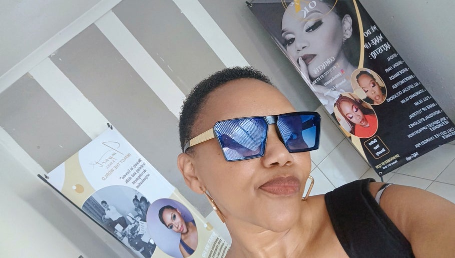 A stylish individual wearing sunglasses at MX-LOOK salon in Soweto, Gauteng, ZA, with beauty posters in the background.