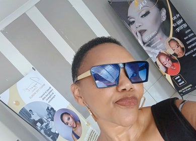 A stylish individual wearing sunglasses at MX-LOOK salon in Soweto, Gauteng, ZA, with beauty posters in the background.
