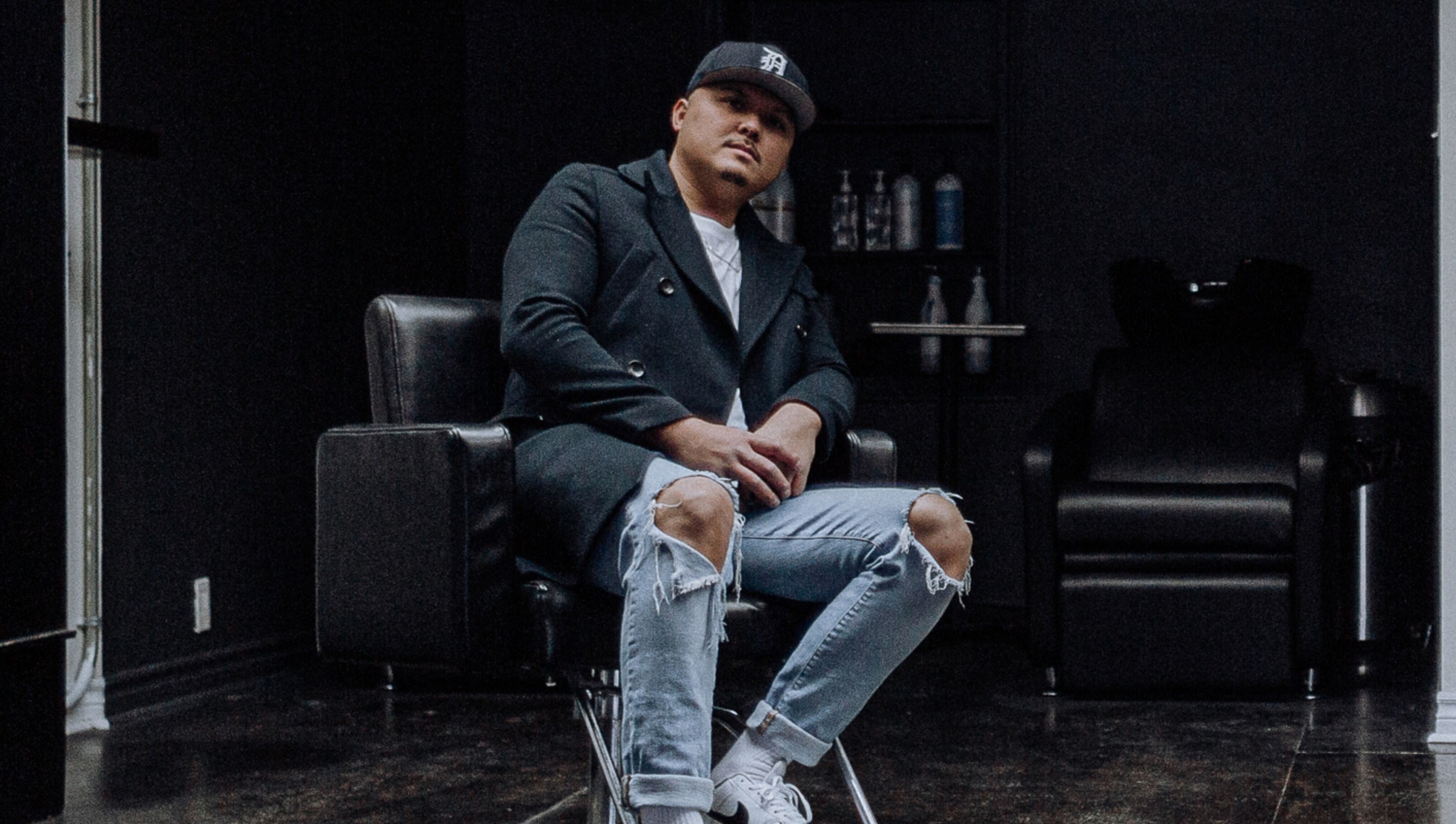 Stylish barber at Barber Stylist Ben, Windsor, Ontario, CA, seated on modern chair with salon backdrop.