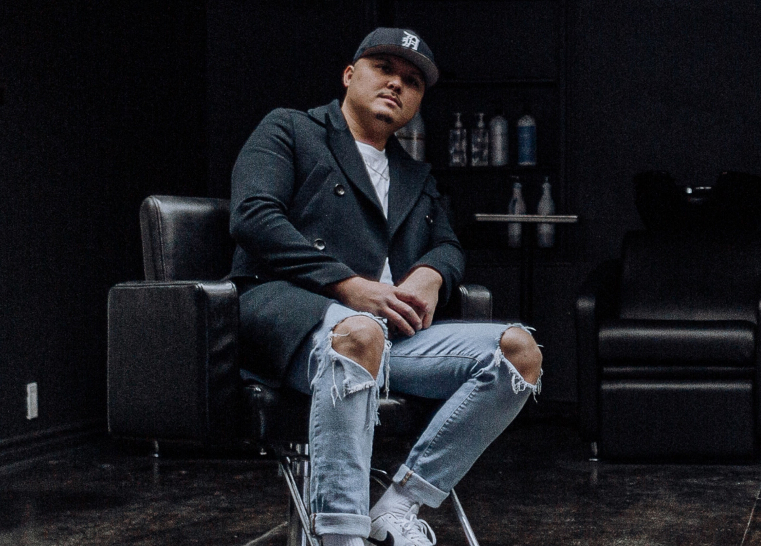 Stylish barber at Barber Stylist Ben, Windsor, Ontario, CA, seated on modern chair with salon backdrop.
