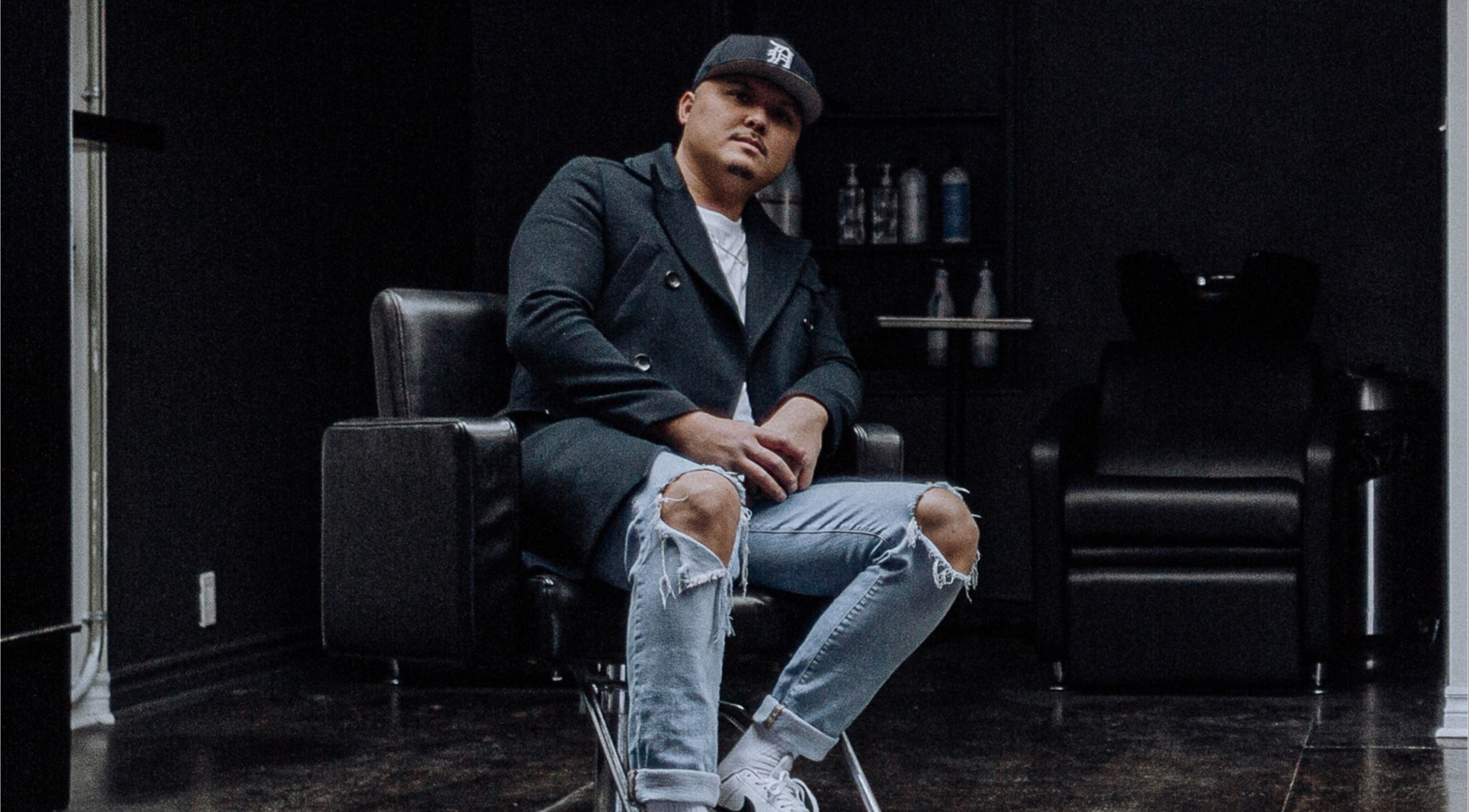 Stylish barber at Barber Stylist Ben, Windsor, Ontario, CA, seated on modern chair with salon backdrop.