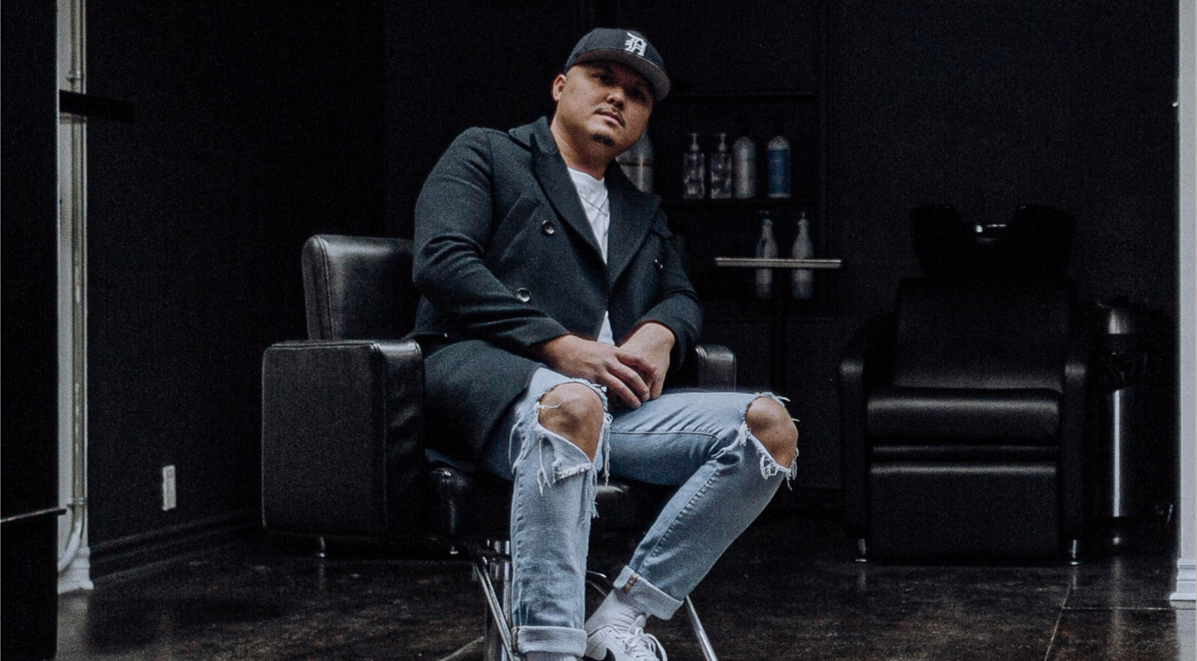 Stylish barber at Barber Stylist Ben, Windsor, Ontario, CA, seated on modern chair with salon backdrop.
