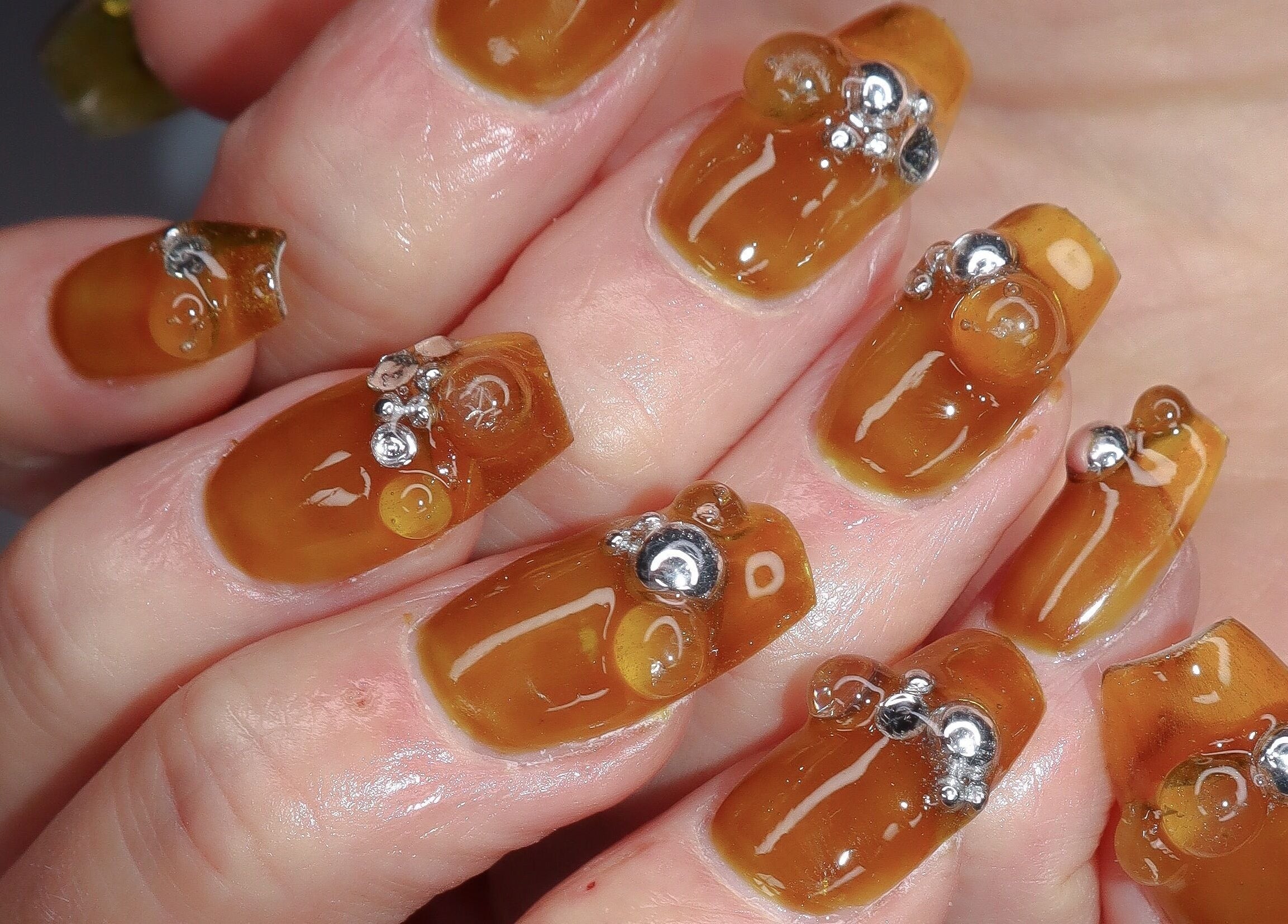 Close-up of elegant amber nail design with silver accents at Yanice Gianina Nails, Berlin, Berlin, DE.