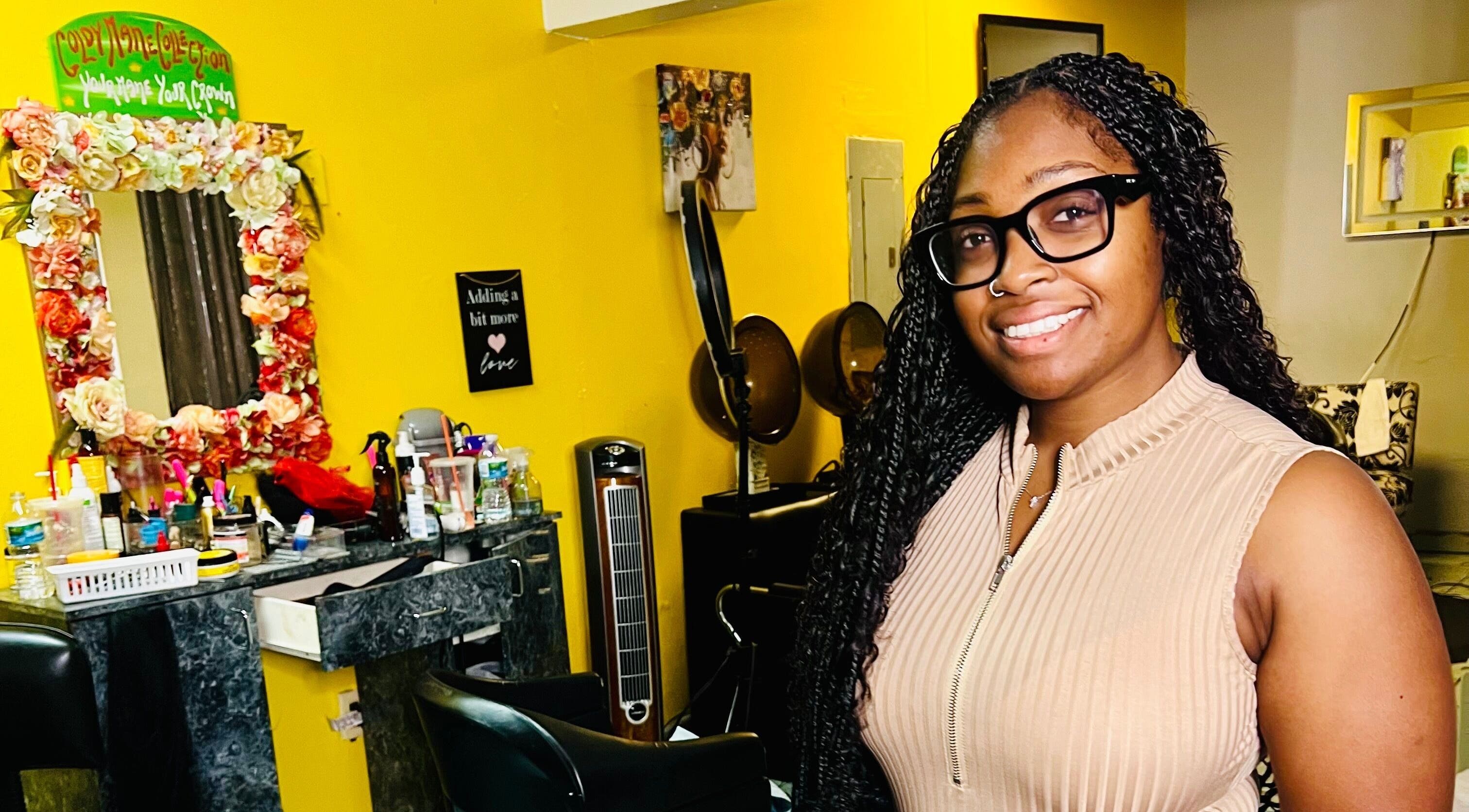 Smiling professional in Goldy Mane Collection salon, Miami, Florida, US. Vibrant decor in the background.