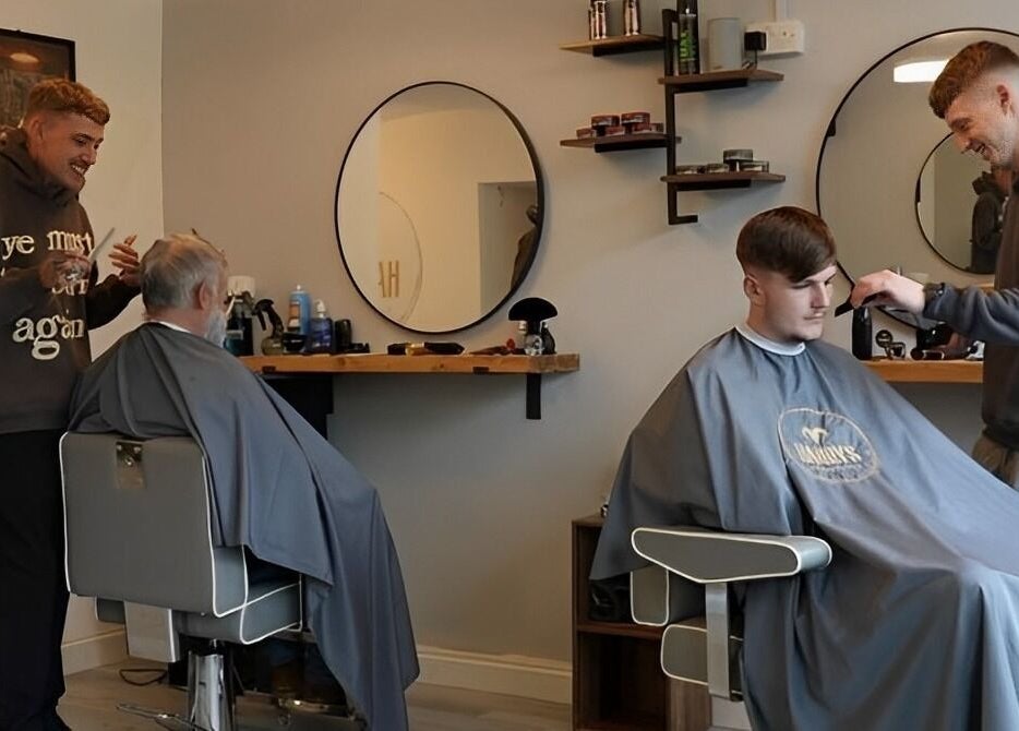 Barbers styling hair at Harry’s Barbershop, Ramsbottom, England, GB. Modern mirrors in the background.
