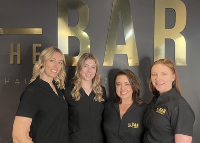 Team at The Bar Hair Body Beauty in Penrith, New South Wales, AU posing in front of salon logo.