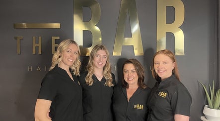 Team at The Bar Hair Body Beauty in Penrith, New South Wales, AU posing in front of salon logo.