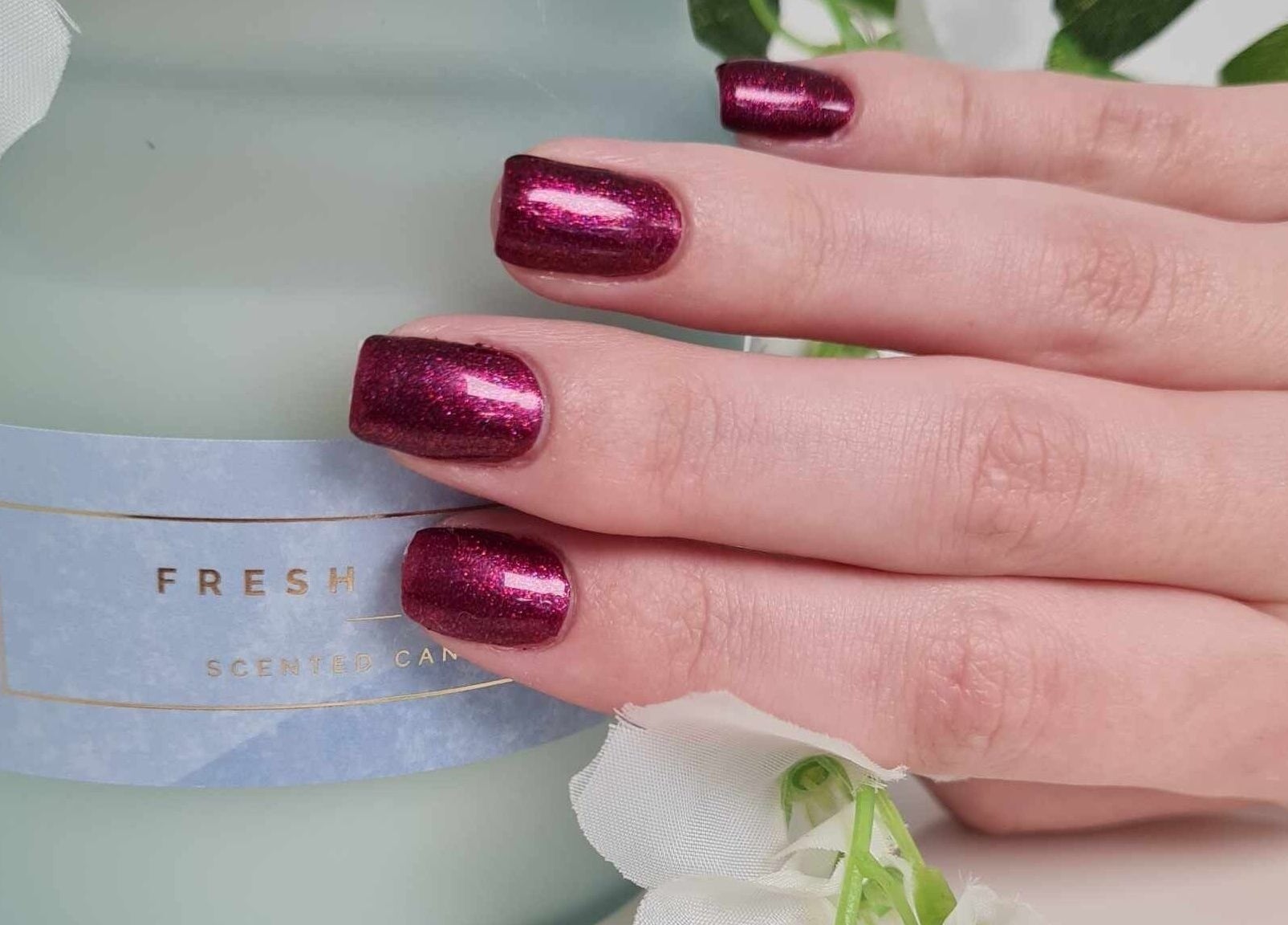Elegant maroon nails by Blissful Touch, Bugle, England, GB, resting on a scented candle.