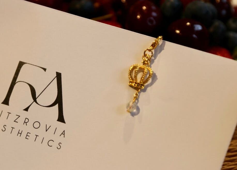 Gold crown charm on Fitzrovia Aesthetics card, London, England, GB. Symbolizes luxury and beauty services.