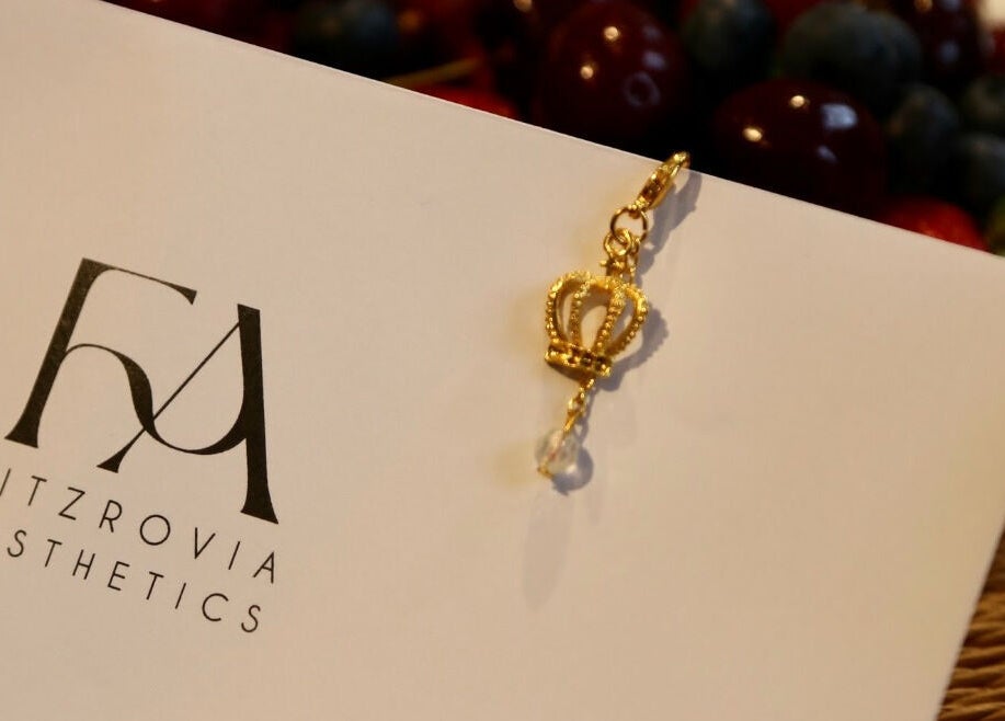 Gold crown charm on Fitzrovia Aesthetics card, London, England, GB. Symbolizes luxury and beauty services.
