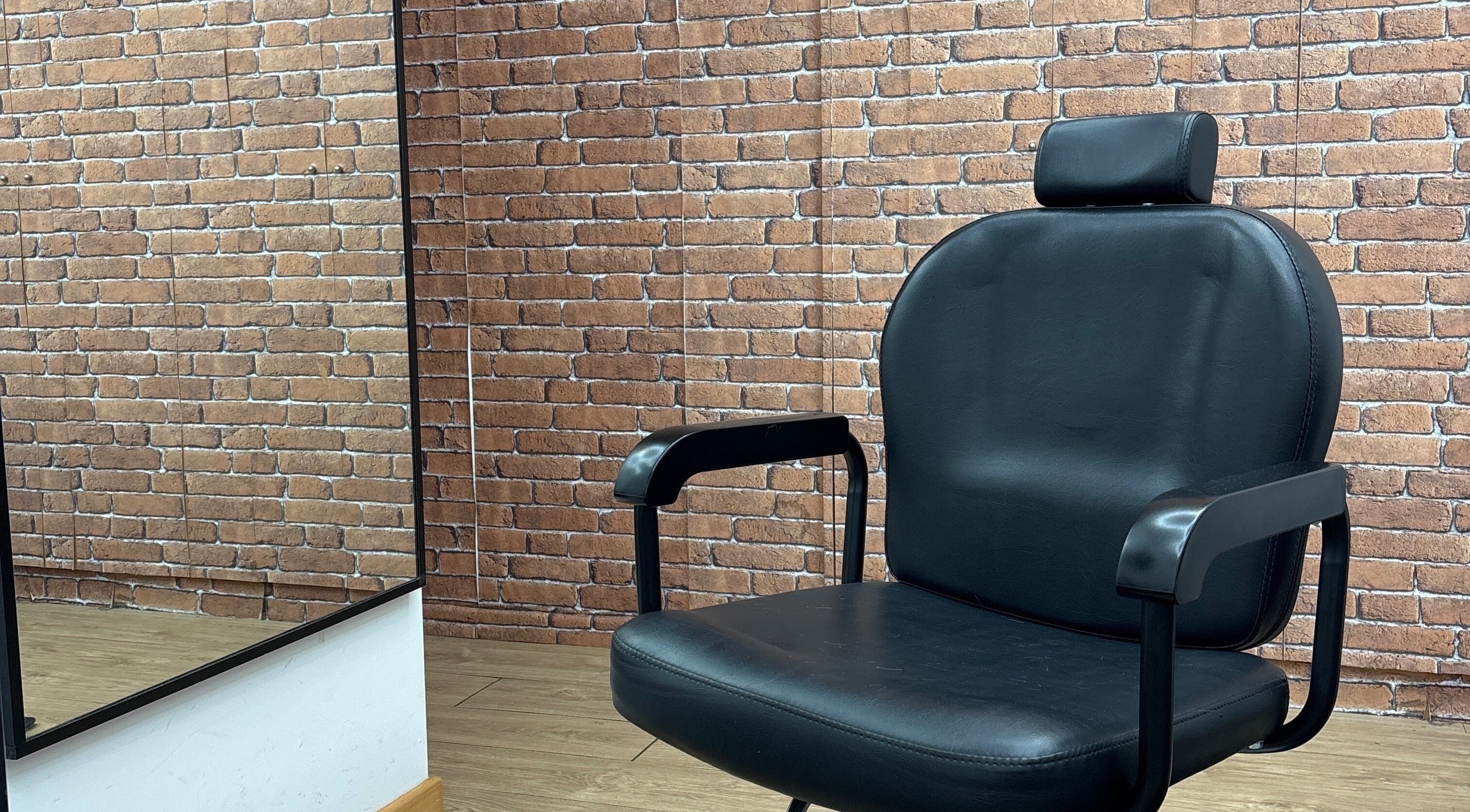 Cadeira de barbeiro em couro preto no Fratucelli Barbershop, Braga, Braga, PT, com fundo de tijolos expostos.