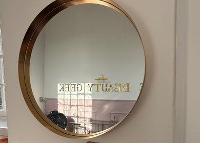 Elegant round mirror reflecting Beauty Geek UK interior in Paisley, Scotland, GB, creating a bright, welcoming ambiance.