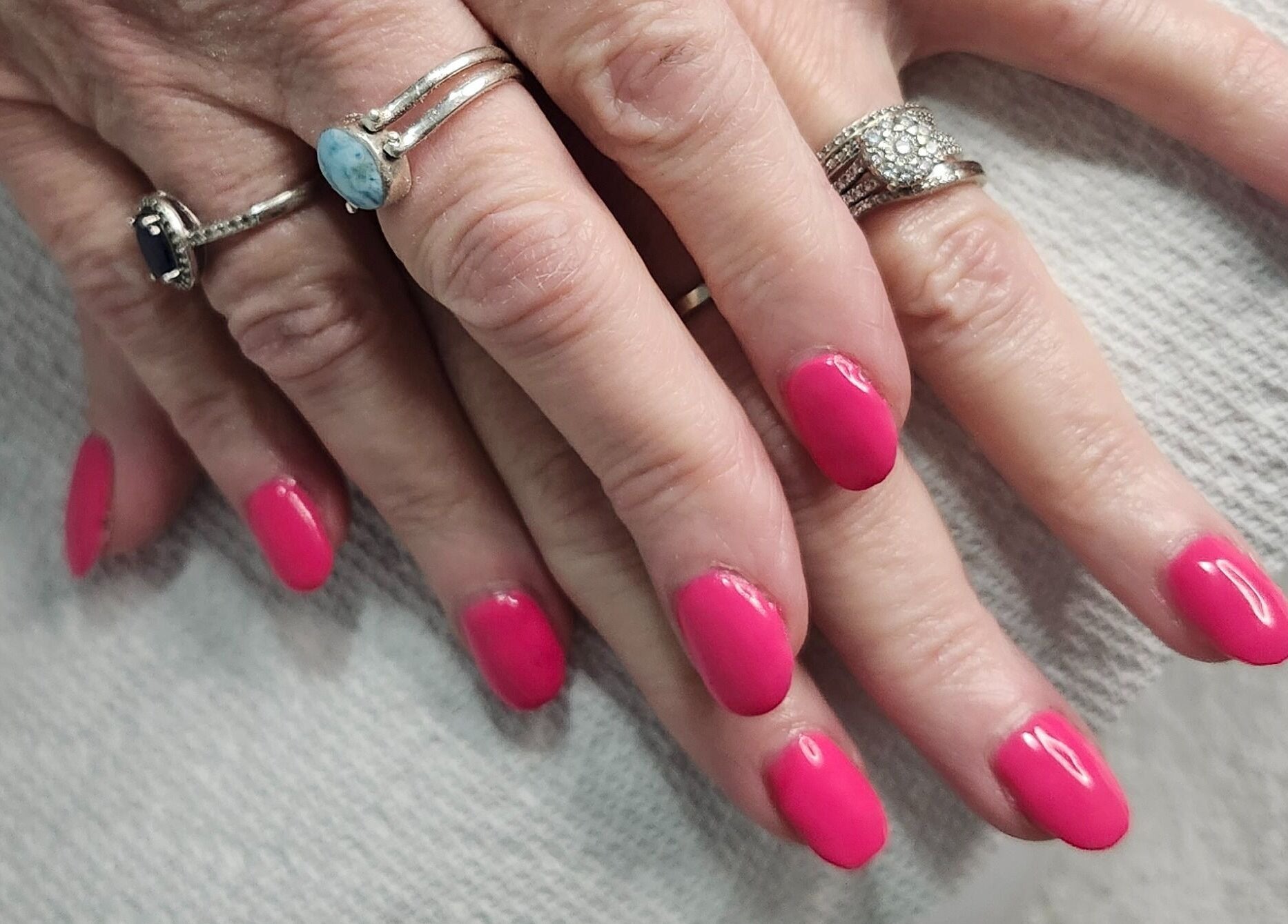 Vibrant pink nails with elegant rings at Opulence Nails, Middle Sackville, Nova Scotia, CA.