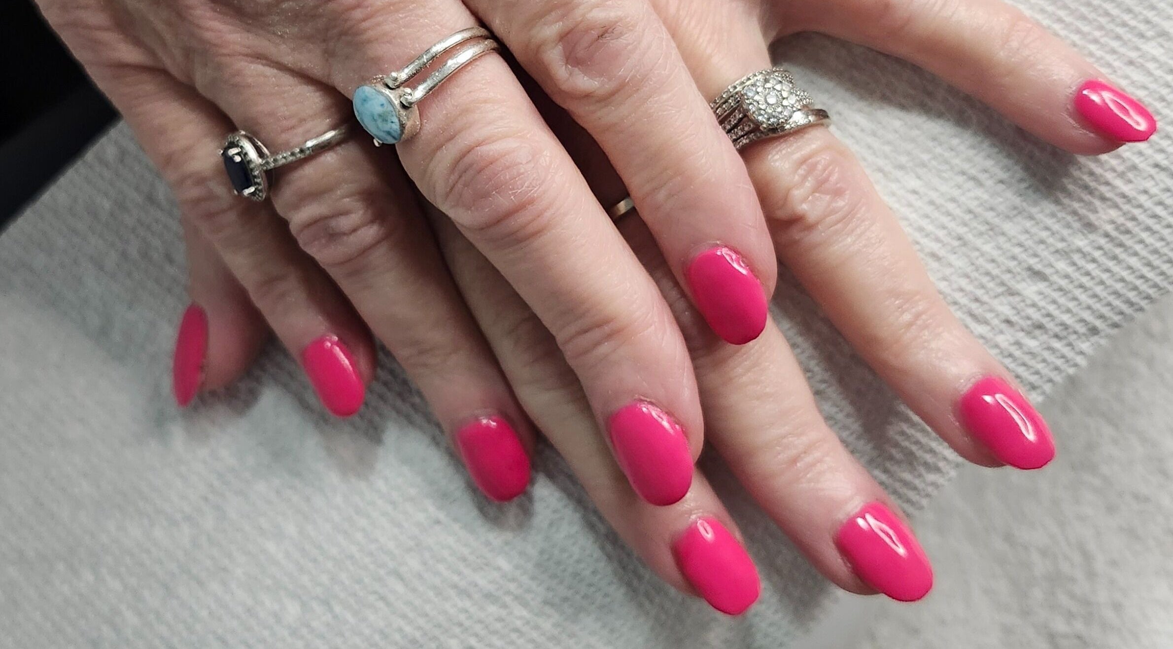 Vibrant pink nails with elegant rings at Opulence Nails, Middle Sackville, Nova Scotia, CA.