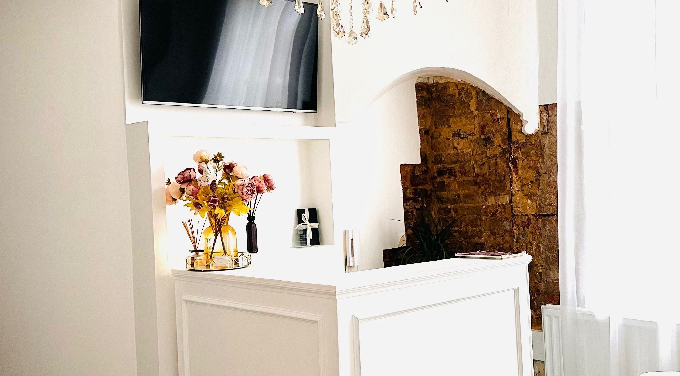 Reception area at MK Aesthetics Clinic in Derby, England, featuring a white desk and floral decor.